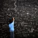 Young boy writes math equations on chalkboard