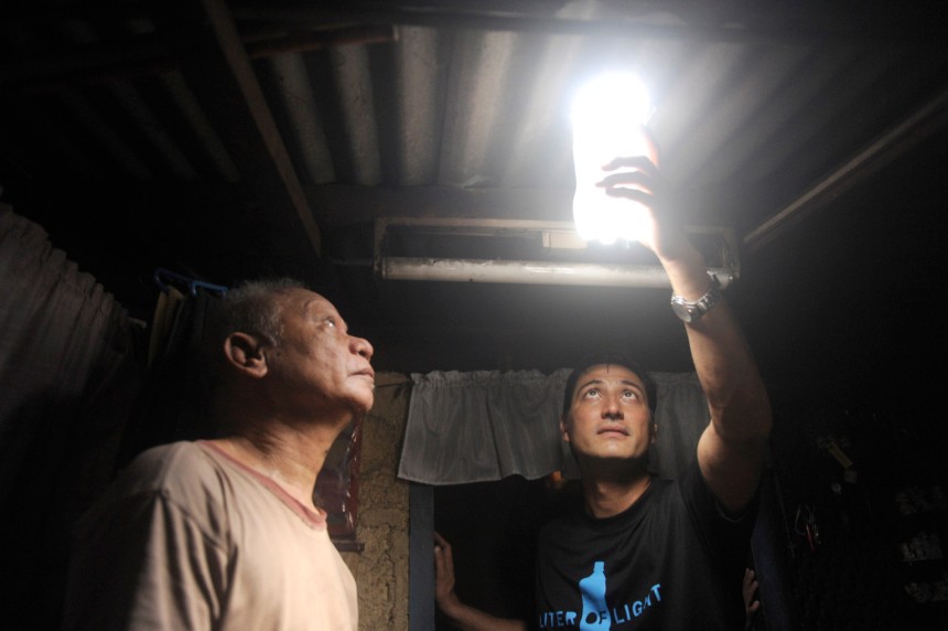 TO GO WITH AFP STORY by Karl Malakunas   -   FILES   -   Illac Diaz (R) inspects a solar light bulb with Siplicio Mondas, 73, installed by the Philippine army soldiers on a roof in a shanty town in Manila, with other private and government organization, they hope to install simultaneously around 10,000 solar bottle bulbs in the slum aria in Metro Manila on November 30, 2011 in a project called "Liter of Light".   Filipino social entrepreneur Illac Diaz is aiming to help a million poor people in a year, and with the help of some plastic bottles plus a savvy social media campaign may do even better. Diaz's project appears simple -- fill discarded soft drink bottles with water, place them in roofs of houses and allow the refracted light to brighten homes during the day instead of using electric bulbs.   AFP PHOTO / JAY DIRECTO (Photo credit should read JAY DIRECTO/AFP/Getty Images)